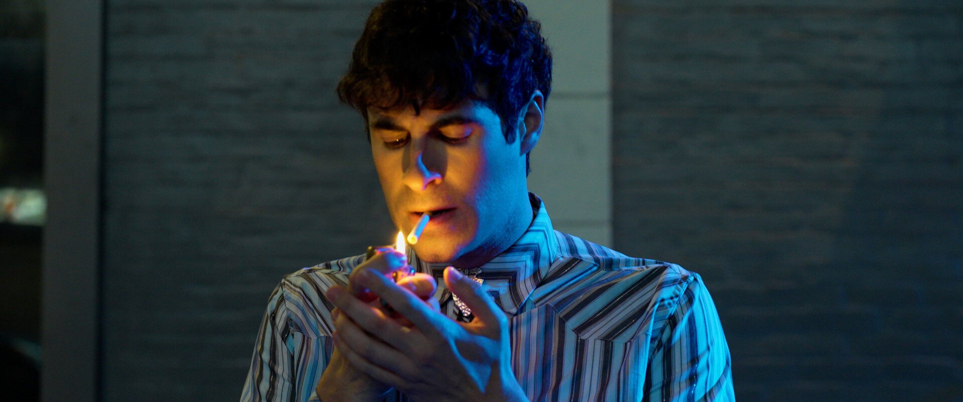 Person lights cigarette in low light lights something in mouth.